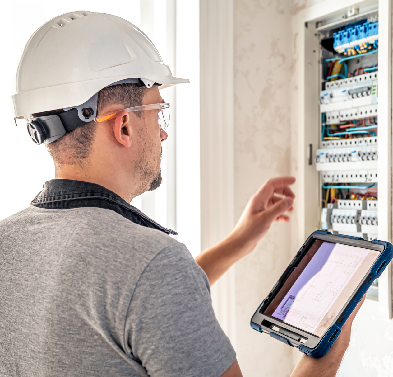 photo of a man wearing a white hard hat checking an electrical panel