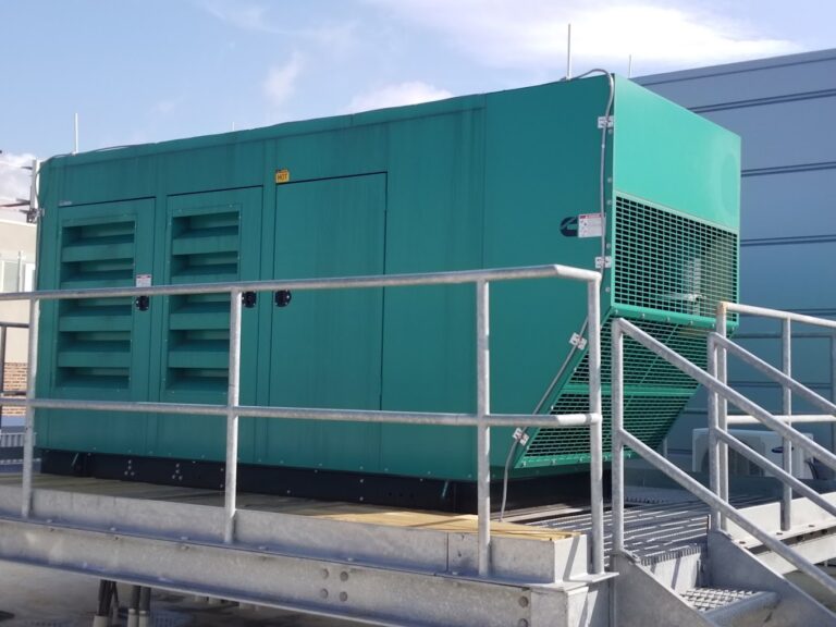 photo of a commercial generator surrounded by fencing. The generator is a teal green color.